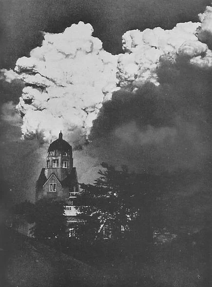 A black and white photograph of huge cloud of smoke looming over domed tower, from the fires of the Great Kanto earthquake in Japan
