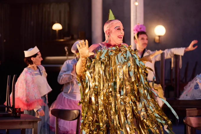 Toby Belch in a gold dress, a wig cap and a party hat.