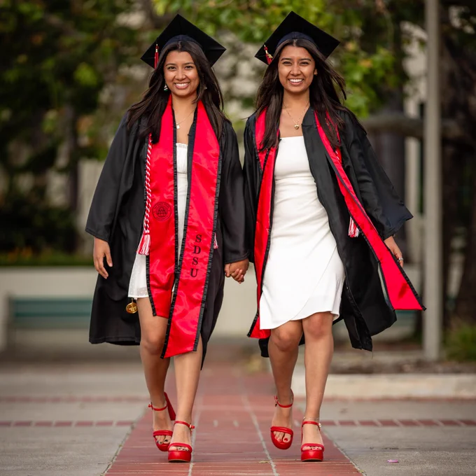 Identical twins Sabrina and Sydney Moreno walk on the SDSU campus wearing caps and gowns.