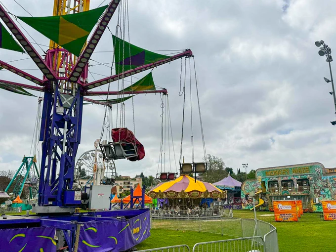 Carnival rides on a green lawn and a cloudy sky.