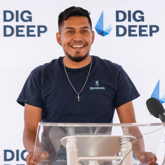 Photo of Jack smiling at a podium against DigDeep background. 