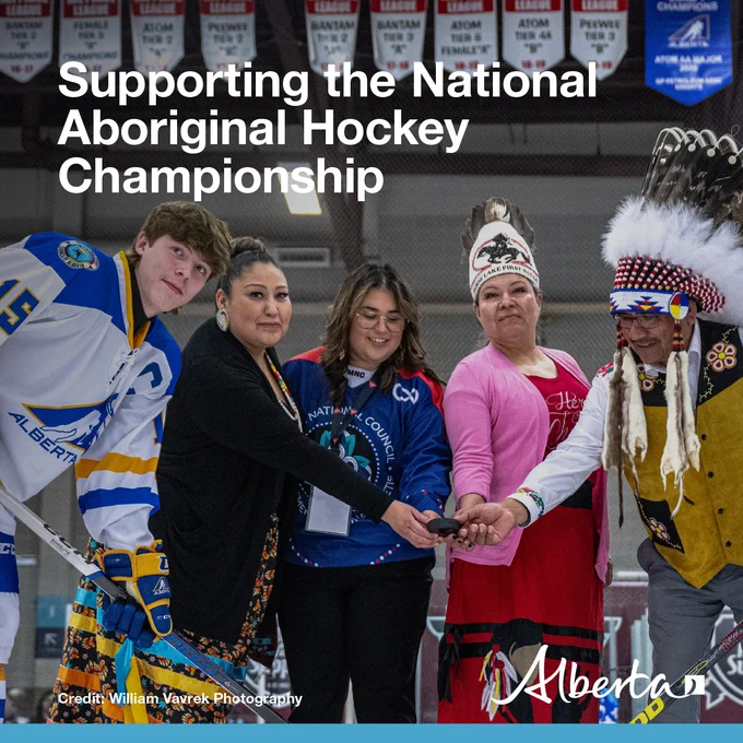 Image displays a group of four Indigenous elders holding a hockey puck and a hockey player during the beginning of a hockey game. Government of Alberta logo at the bottom right.
Text: Supporting the National Aboriginal Hockey Championship. Credit: William Vavrek Photography
