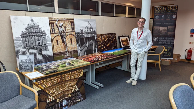 A man standing next to a display of large photographic prints of Oxford.