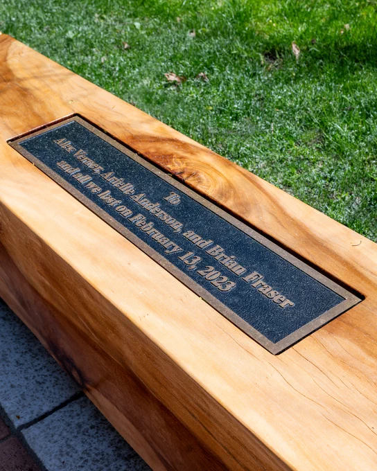 Closeup of a bench with a plaque on it that says To Alex Verner, Arielle Anderson and Brian Fraser and all we lost on February 13, 2023