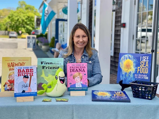 Jenna Grodzicki sitting at a table outside with her children's books on the table in front of her 