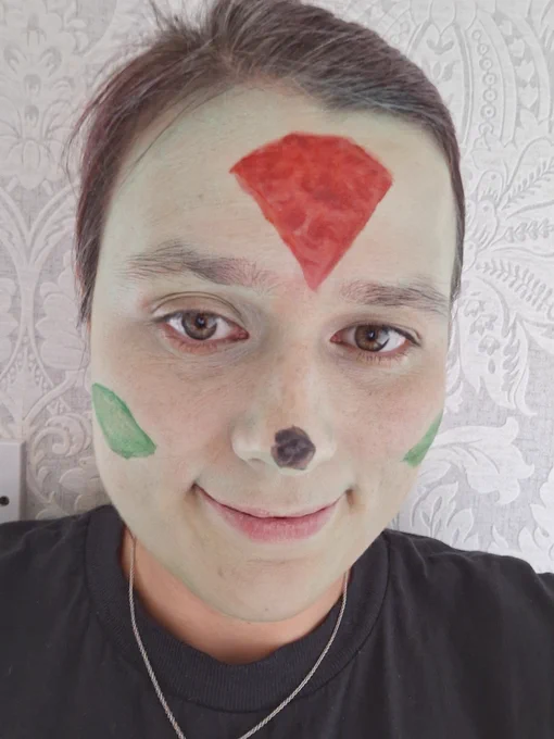 A woman with her face painted with a red diamond on her forehead and green ovals on her cheeks.