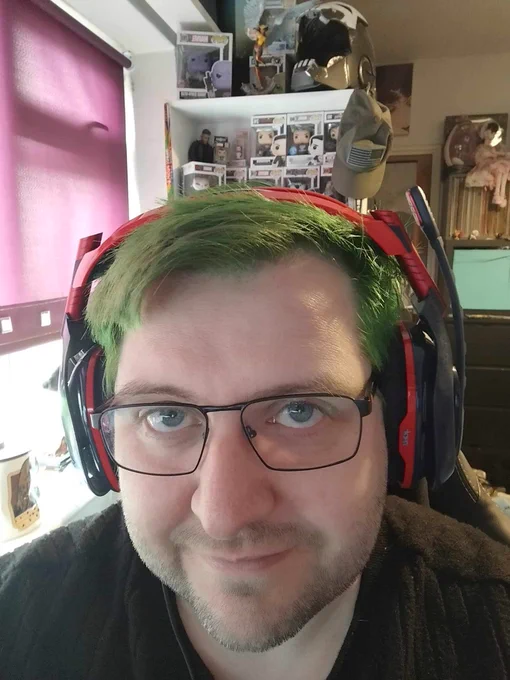 A man with dyed green hair wearing glasses and a gaming headset.