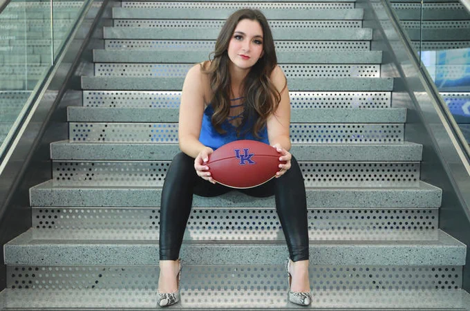 Emily Fields sitting on steps holding a University of Kentucky branded football
