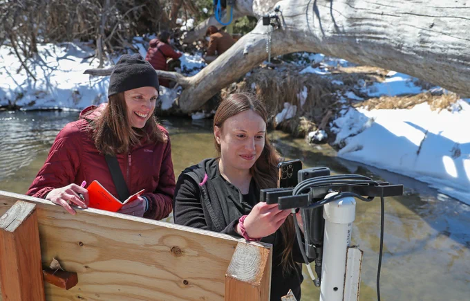 Mary Harner (left), a UNK professor, and Jamila Bajelan, research technician, measure water quality next to a GaugeCam used to measure water levels in the creek at the Kearney Outdoor Learning Area. The work is part of the GRIME Lab research.
