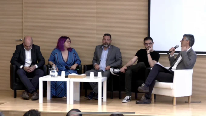 En el escenario con los otros cuatro ponentes todos sentados alrededor de una mesa blanca