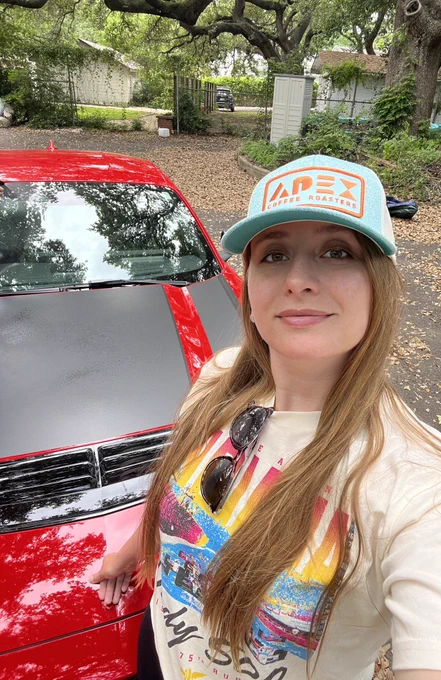 A selfie of Alanis in an Apex hat with a red Mustang Dark Horse.