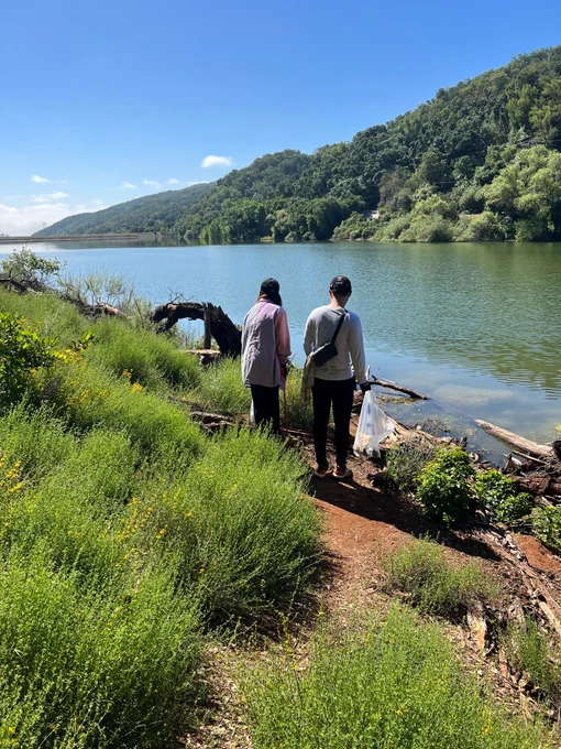 a lake landscape photo. Two people are on the shore of the lake with their backs to the camera. one is holding a bag