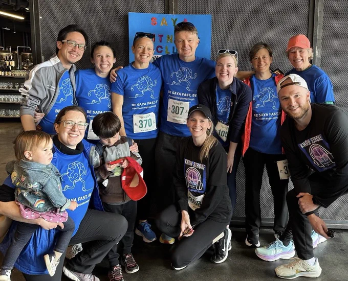 Group of smiling people wear bright blue shirts for their fitness club and bibs for a 5K.