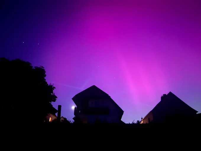 Violet Northern Lights behind a dark silhouette of roof tops.