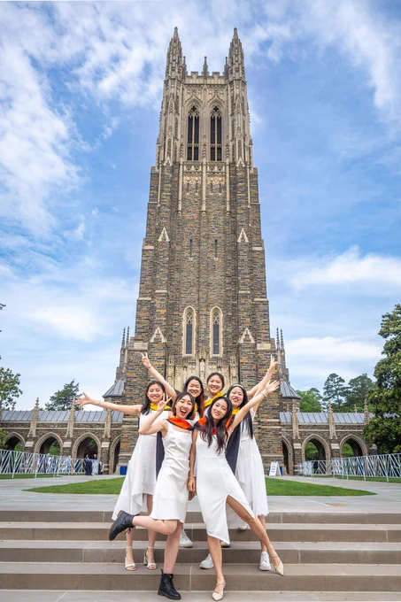 A group of six graduates pose in white dresses in front of the chapel.