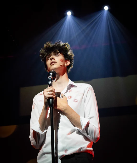 student singing into mic, backlit by stage lighting