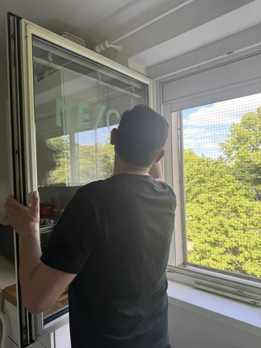 Mann mit schwarzem T-Shirt steht in Küche und schreibt mit Stift auf offenem Fenster