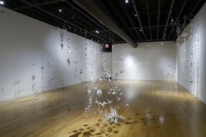 A photograph of a wire chandelier caught in wires and threads in the centre of a gallery. 

