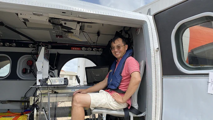 Zhien Wang (an East Asian man in a t-shirt and shorts) poses in a Twin Otter aircraft.