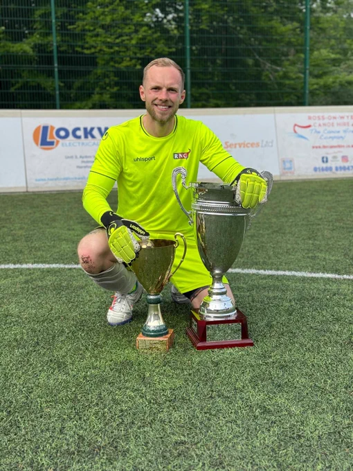 Me on the pitch crouched down with the National League Trophy and the Brian Aarons Cup.