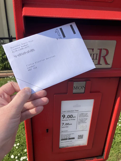 Photo shows hand posting letter in red postbox.