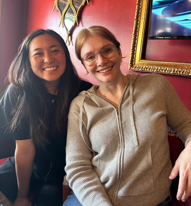 Sitting in a booth, Moet (left) and BDH (right) smile after a delicious Mother’s Day brunch. Moet wears a black blouse and slacks with her long black hair down, and BDH wears a grey knit hoodie, jeans, and her hair pulled back in a bun.