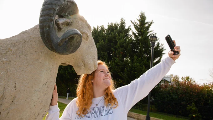 Shepherd University student takes selfie with Ram Statue outside Ram Stadium.