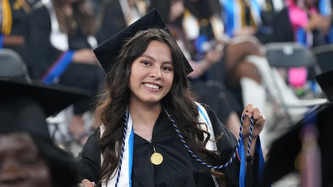 student graduating holding blue and white tassel