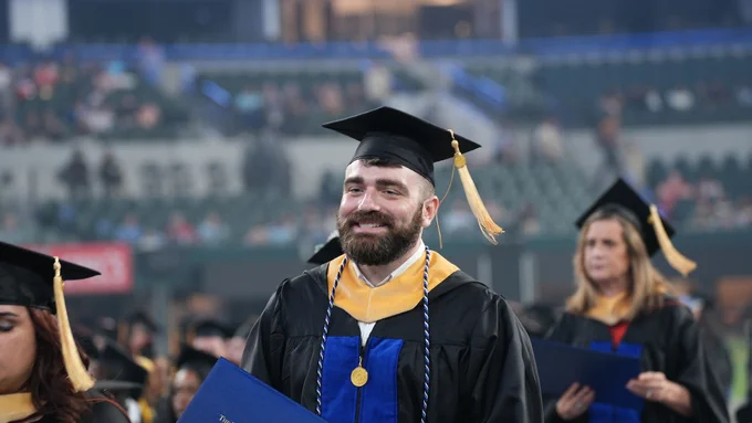 student smiling with Social Work hood, and blue and white tassel