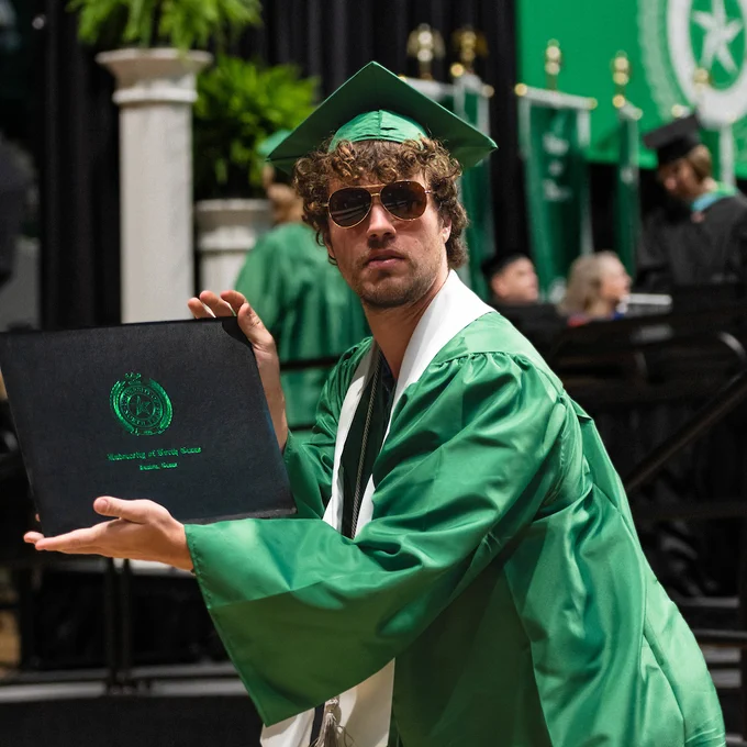 Graduate holding their diploma cover at a UNT Spring 2024 commencement ceremony.
