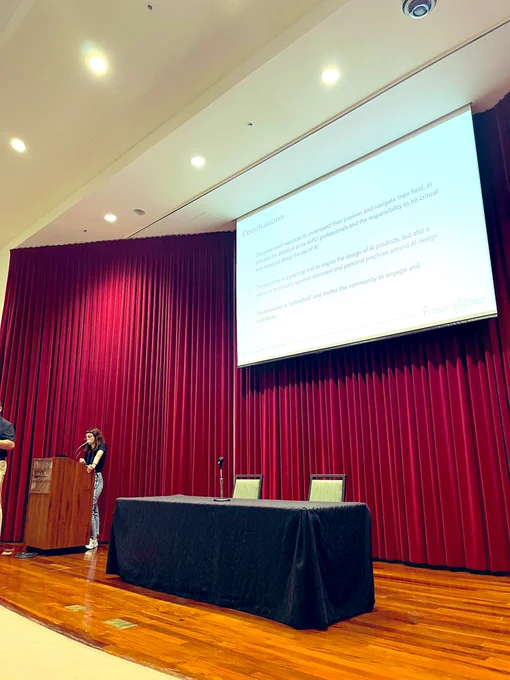 A woman is standing and giving a talk with the slide showing in the back