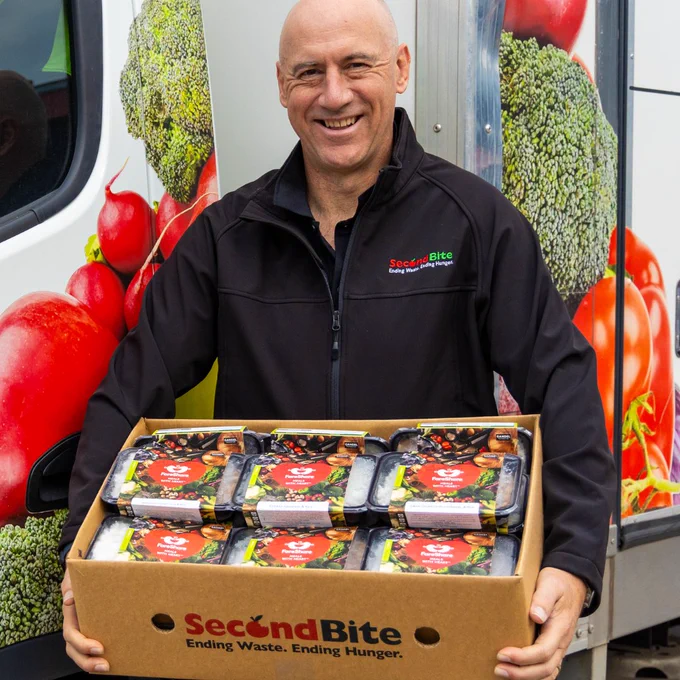 SecondBite CEO Daniel Moorfield, pictured smiling holding a SecondBite Box full of FareShare meals. 