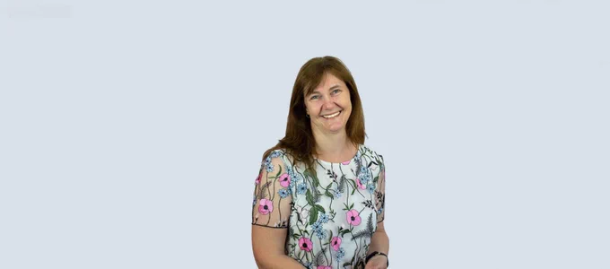 Headshot of Julie. She has shoulder-length brown hair and is wearing a white t-shirt with pink and blue flowers. 
