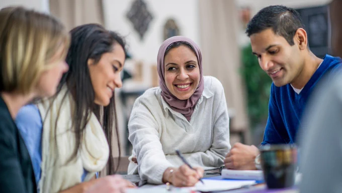 A group of four smiling people sitting at a table and working