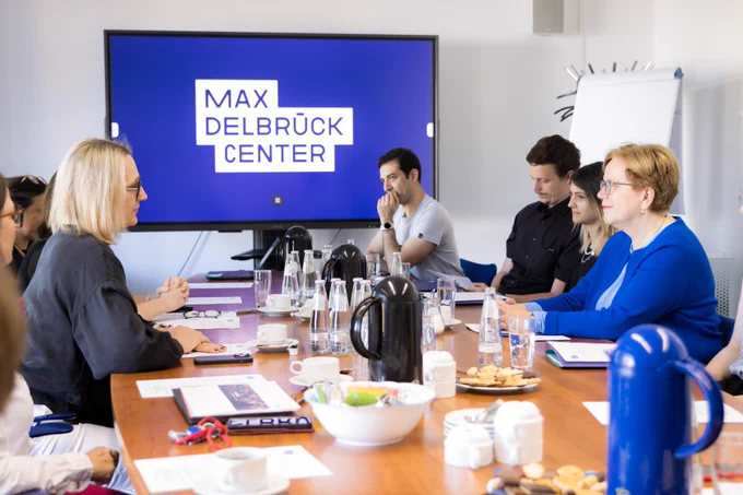 In the foreground, this photo shows Maike Sander (Scientific Director of the Max Delbrück Center) and Gabriele Bischoff (politician and member of the European Parliament) in a conference room. Other people are in the background, where a large TV screen depicts the Max Delbrück Center logo in white on a blue background. © Felix Petermann, Max Delbrück Center