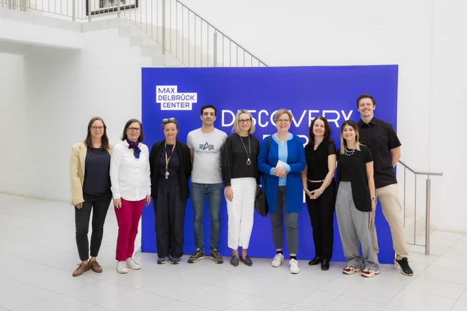 A group photo showing nine people standing in front of a blue photo wall with a logo of the Max Delbrück Center. Among the people are Maike Sander (Scientific Director of the Max Delbrück Center), Heike Graßmann (Administrative Director of the Max Delbrück Center), Gabriele Bischoff (politician, member of the European Parliament), as well as other administrative staff and scientists. © Felix Petermann, Max Delbrück Center