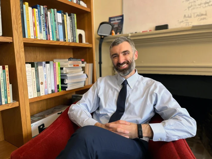 Kevin Elliott seated in his office, next to a bookcase and in front of a fireplace