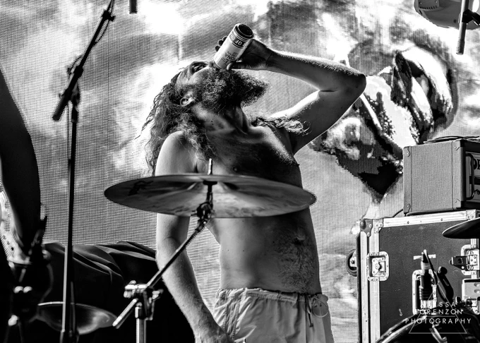 Photo by Alyssa Lorenzon / TJ, a shirtless bearded long haired rock’n’roll man, drinks a beer behind his drum kit