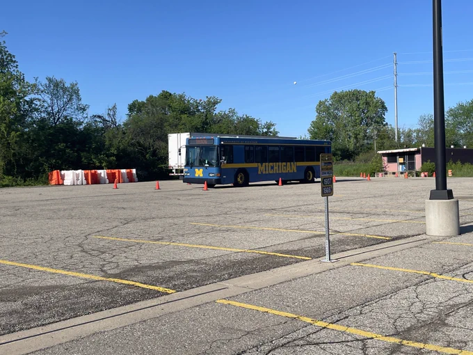 A large blue bus practicing with orange cones in a large parking lot.