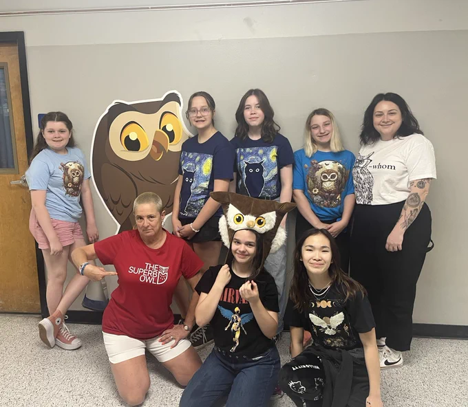 Group of students and adults in owl tshirts with owl decal on wall.