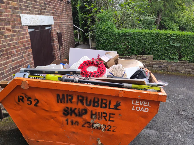 A skip full of lots of things. On the top is a wreath. 