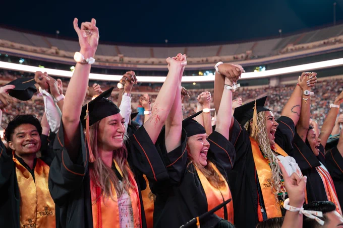 A group of graduates hold hands with each other and raise them up during commencement 
