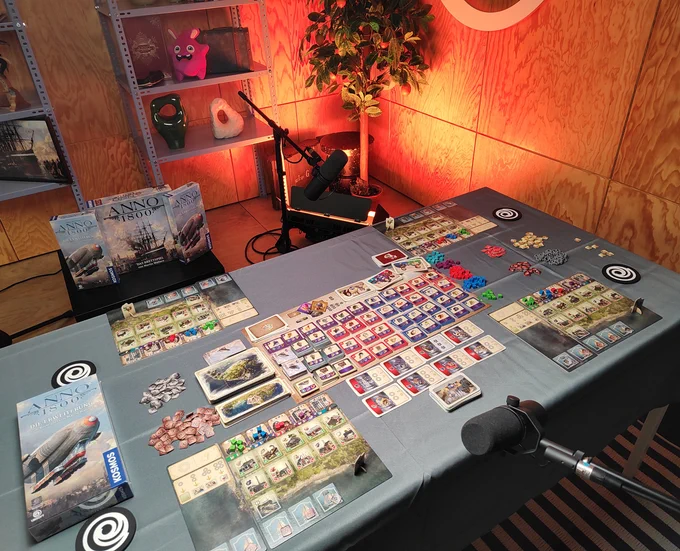 A table with a fully setup play session for the Anno 1800 boardgame, including many cards and maps of the boardgame.
