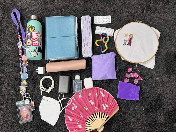 A pile of stuff that was in a con committee person's bag.

— Lanyard (badges optional)
— Water bottle
— Notebook
— Reusable cutlery
— Painkillers (ibuprofen and paracetamol)
— a random fidget toy
— a craft
— reusable tote bag
— full set of dice, just in case
— a fan, because the Jasper’s temperature varies
— a mask
— ear buds
— hand sanitiser
— phone charger (battery and wall)
— phone charging cord
— pen case with highlighters etc