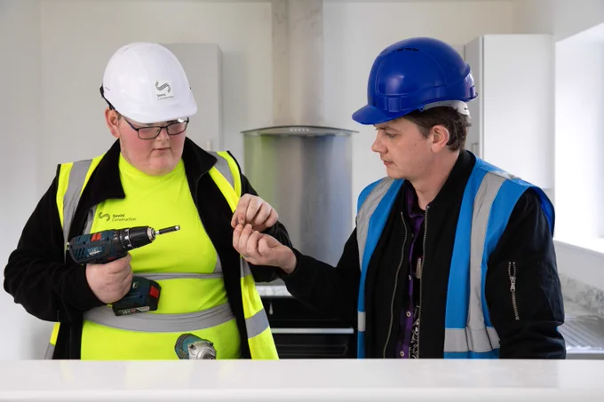 A young man on a supported internship on site with a colleague. He is holding equipment and being passed something by the colleague. Top right is the National Careers Service logo and bottom left reads: "www.nationalcareers.service.gov.uk / 0800 100 900".