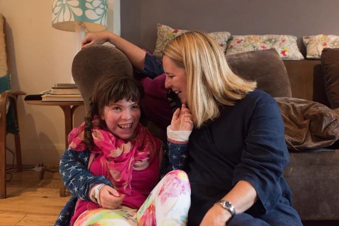 Pic shows Sam with her daughter Elvi in a living room, both are smiling.