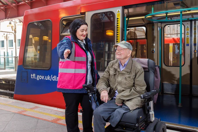 A member of staff from the DLR train posing with a motorised wheelchair user 