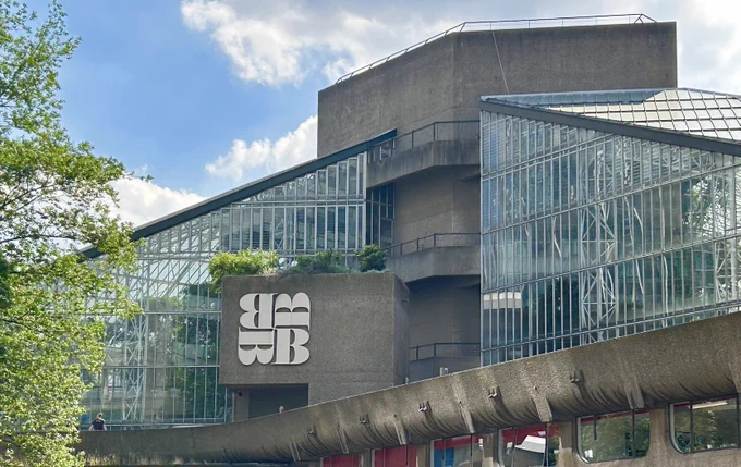The facade of the Barbican centre surrounded by trees and blue sky