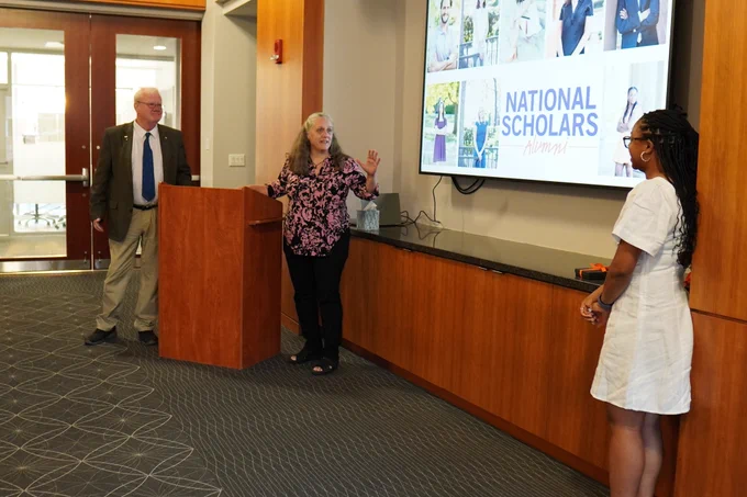 A picture from the dinner, with Dr. Eliza Gallagher and Dr. Neil Calkin at the podium, their student to the right-hand side of the projector screen. 
