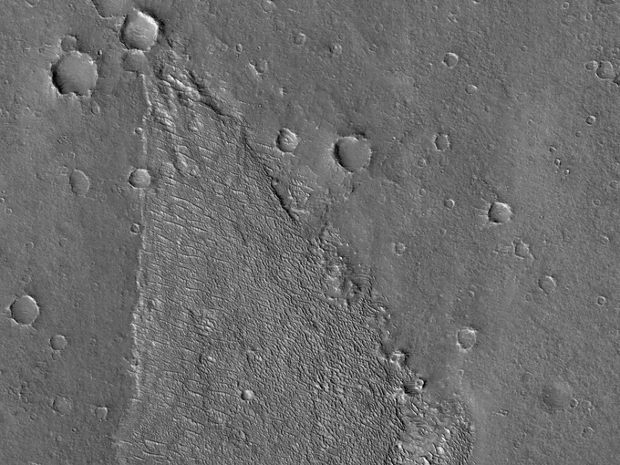 Image shows a large patch of rippled terrain that is distinct from the flatter surrounding terrain where there are also many impact craters of differing sizes. (Credit: NASA/JPL-Caltech/UArizona)